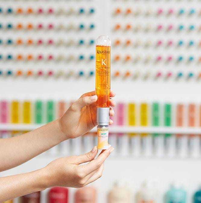 Hands holding Kerastase hair product against a colorful background of hair care items.