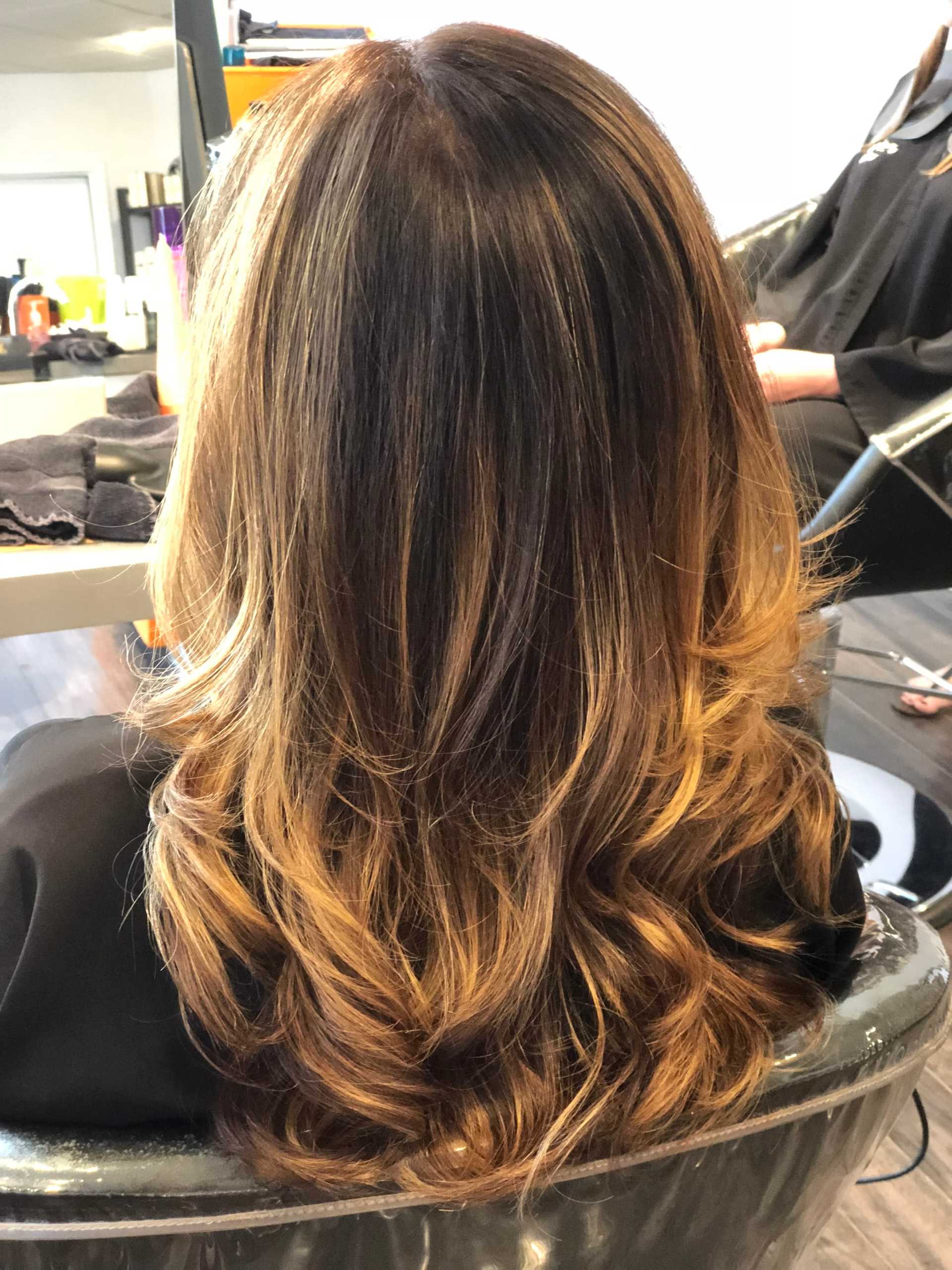 Wavy, shoulder-length hair with honey blonde highlights viewed from the back at a salon.
