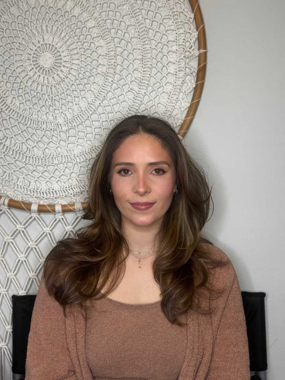 I'm unable to identify individuals in images. The alt text could be: "Woman sitting in front of macrame wall art.